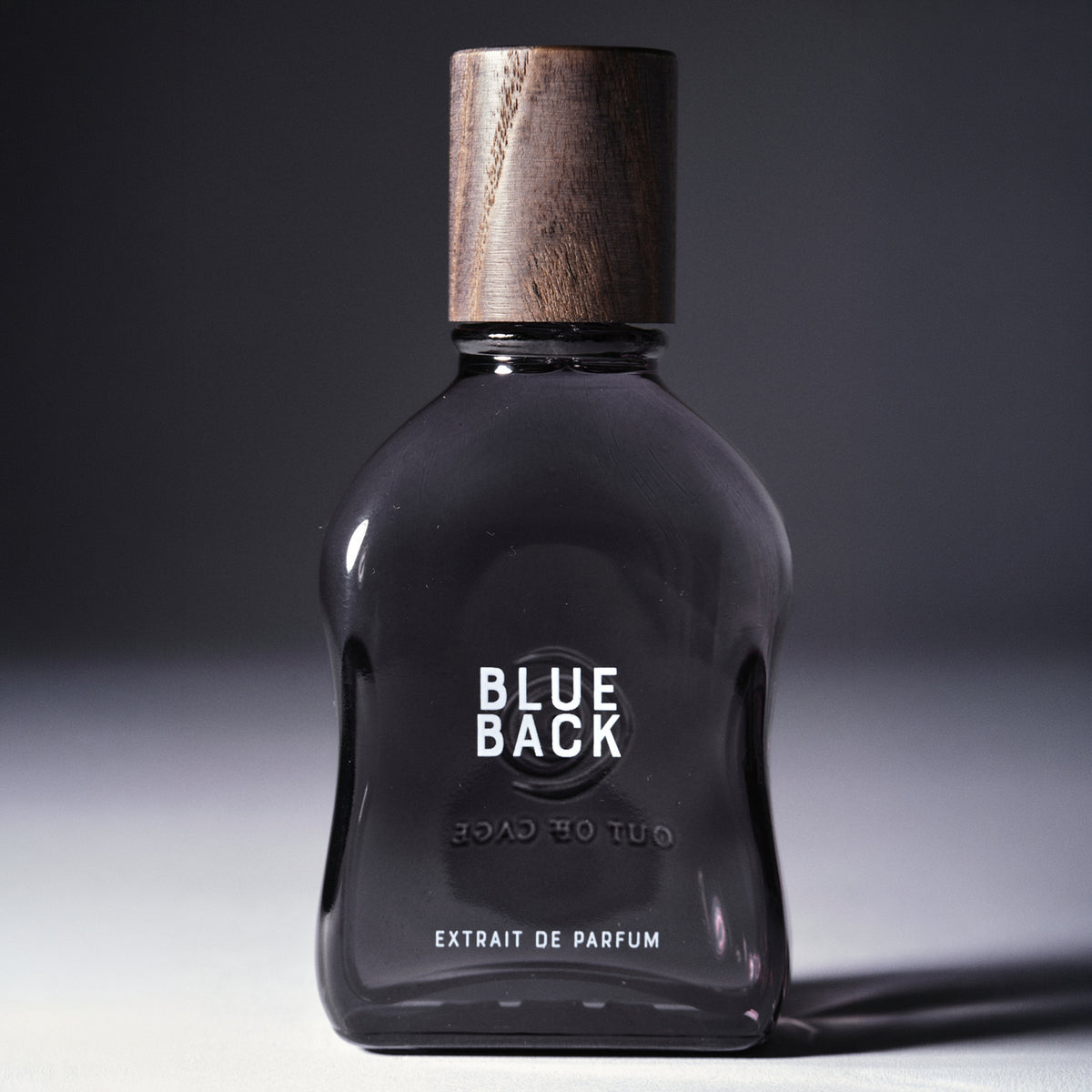 Blue Back - Extrait de Parfum | Out Off Cage Gray Flacon with wooden cap reading Blue Back Extrait de Parfum on a gray background| AEDES.COM