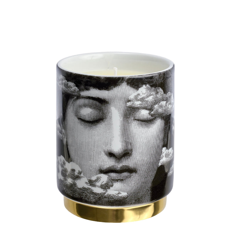 Candle with a black and white design of a face and gold base on a white background