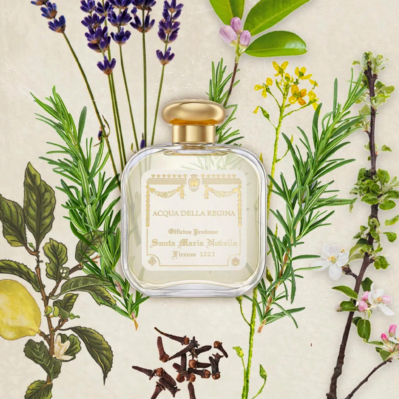 Perfume bottle with gold cap surrounded by herbs and flowers on a light background. Acqua della Regina | Santa Maria Novella | Aedes.com