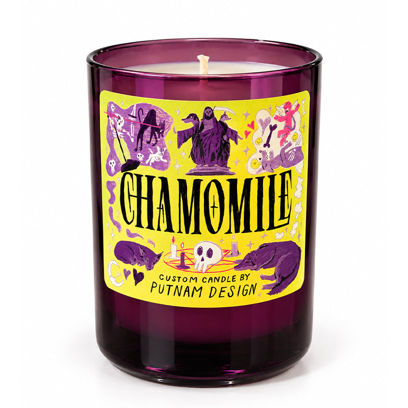 A purple glass jar candle with a bright yellow label featuring gothic illustrations and the word 'CHAMOMILE' in large black letters. The label also reads 'CUSTOM CANDLE BY PUTNAM DESIGN'.