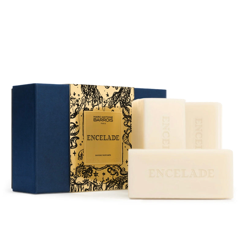 Three cream-colored ENCELADE soap bars displayed in front of their navy blue and gold patterned gift box on a clean white background.