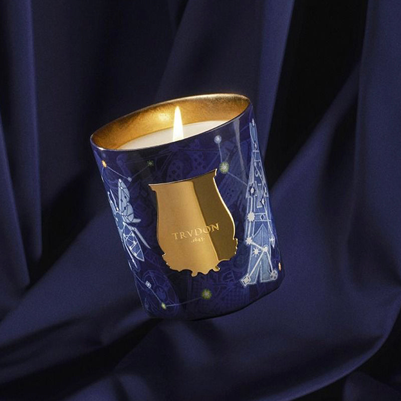 Trudon Luna candle in a decorative navy container with gold accents on a dark blue fabric background