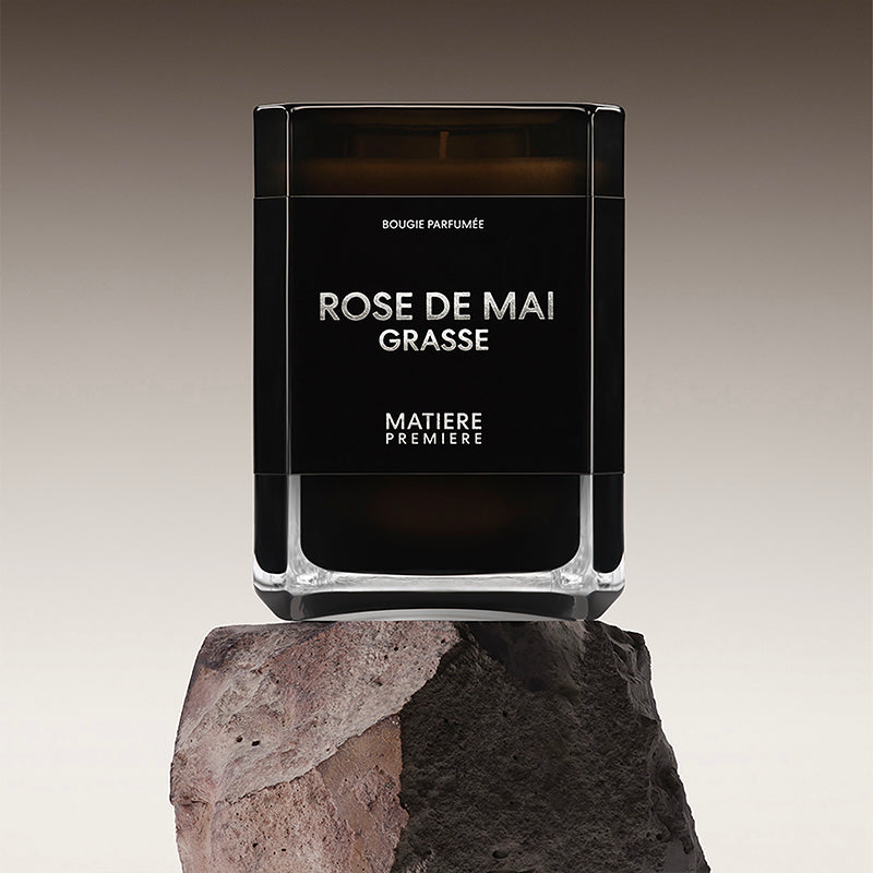 Black candle labeled 'Rose de Mai Grasse' by Matiere Premiere on a stone surface with a gradient background.