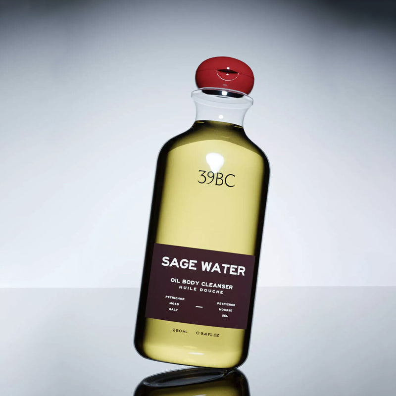 Bottle of Sage Water oil body cleanser with a red cap on a gray background