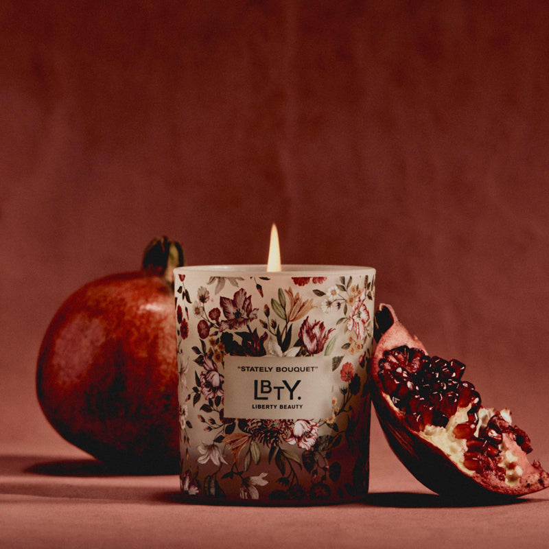 Candle with floral design and 'LBY' branding next to a pomegranate on a brown background