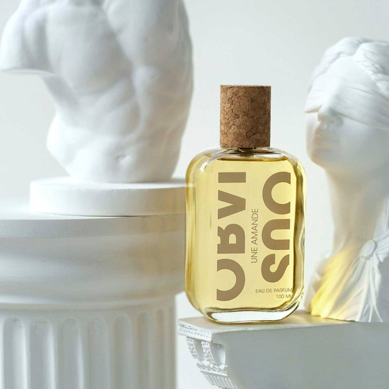 Flacon by Obvious, clear glass with cork cap.Une Amande Eau de Parfum 100ml sitting on a greek plaster column with sculptures.