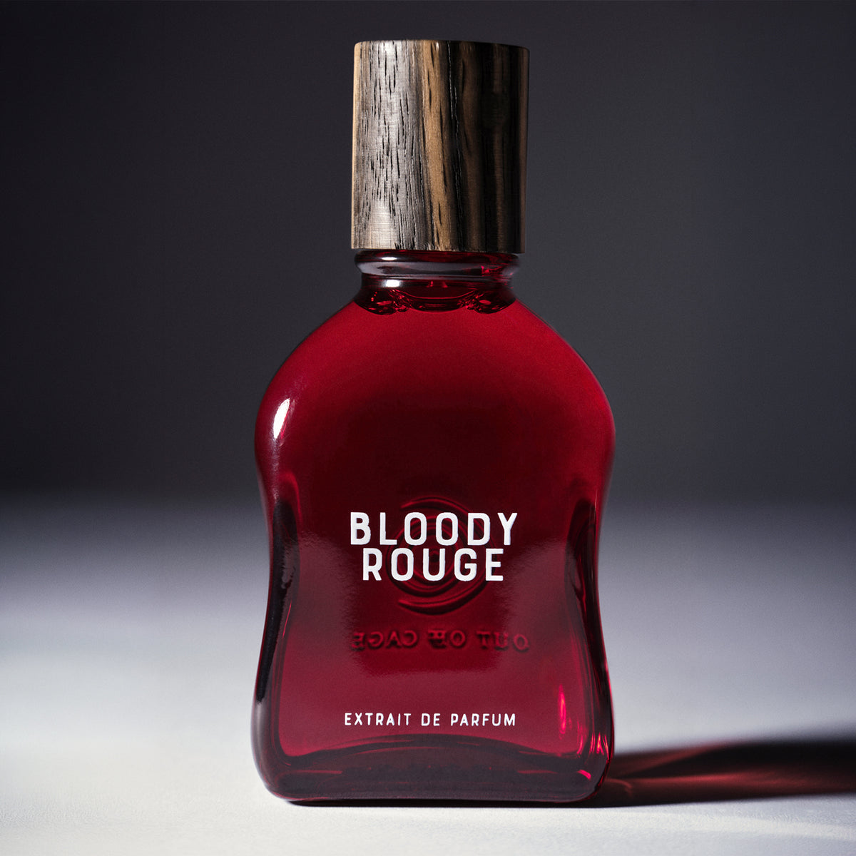 Bloody Rouge - Extrait de Parfum. Image of red flacon with wooden top reading Bloody Rouge Extrait de Parfum with dark background| Out Off Cage | AEDES.COM
