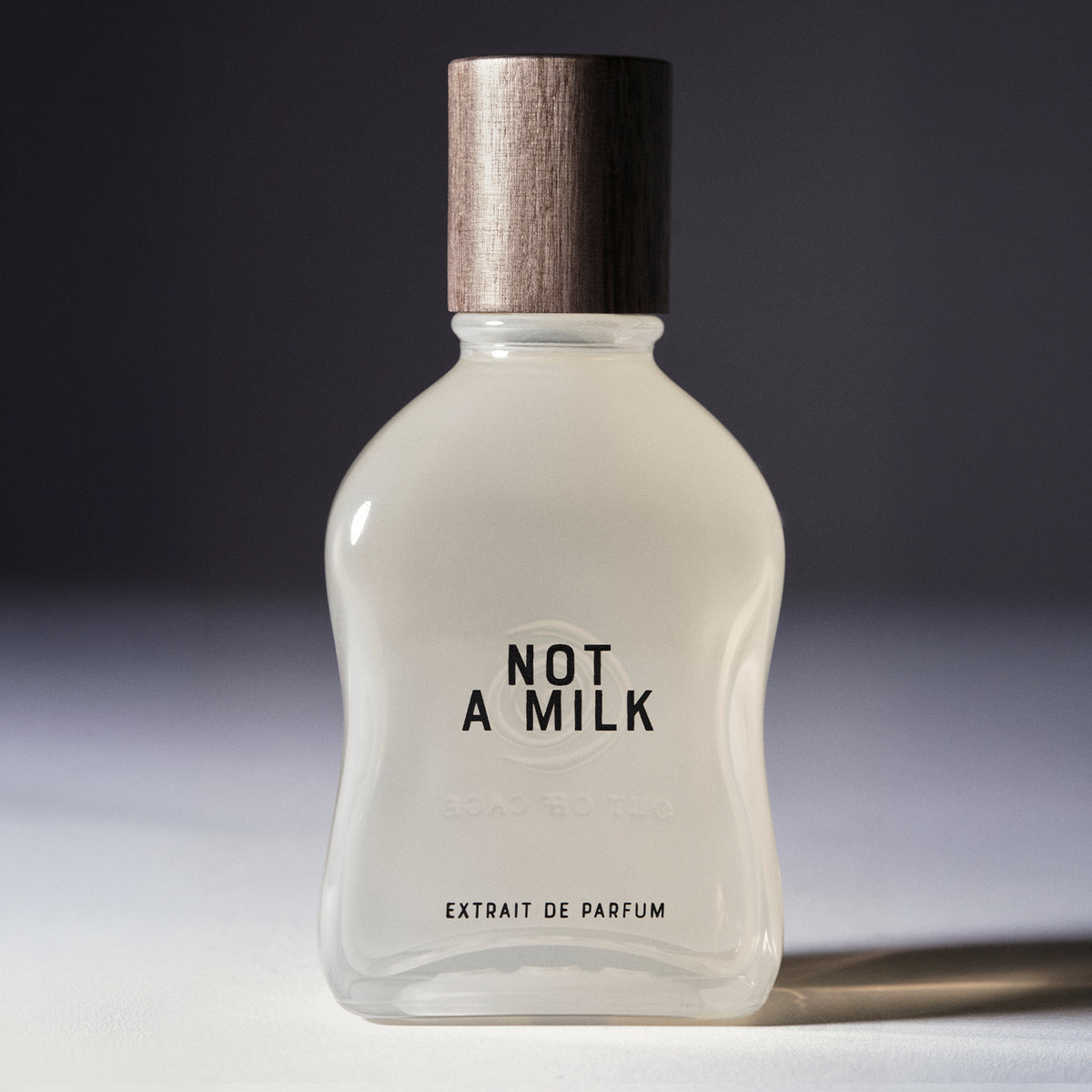 Not A Milk - Extrait de Parfum | Out Off Cage. Frosted white flacon with wooden cap reading NOT A MILK Extrait de Parfum on gray background.  AEDES.COM