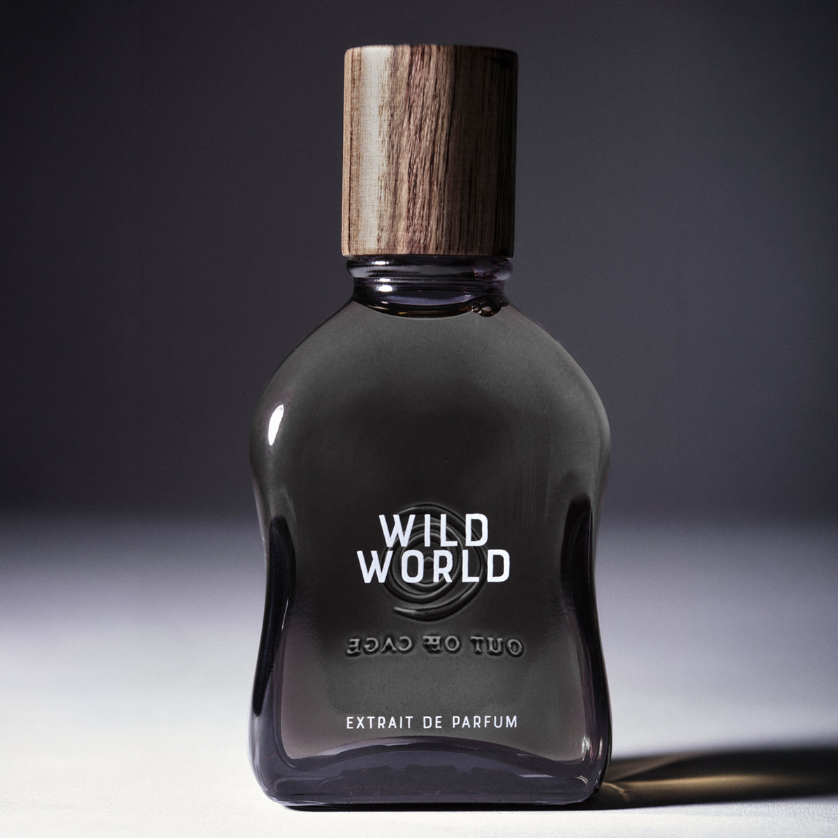 Wild World - Extrait de Parfum | Out Off Cage | AEDES.COM. Gray Flacon with wooden cap reading WILD WORLD Extrait de Parfum on gray backdrop