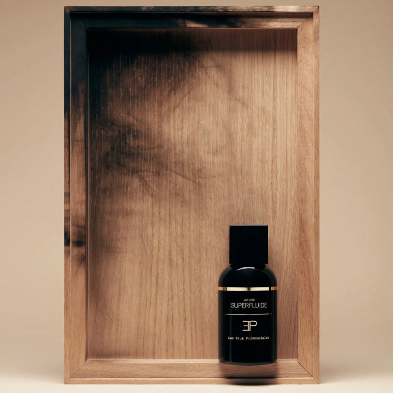 Black bottle with gold text on a wooden tray. Ambre Superfluide EdP - Superfluide Collection | Les Eaux Primordiales

