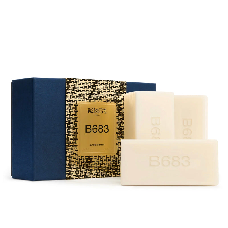 Three cream-colored soap bars with embossed 'B683' markings are displayed in front of their packaging box. The box features a navy blue side and a gold patterned center panel with a gold label reading 'BAZAAR PARIS B683'.