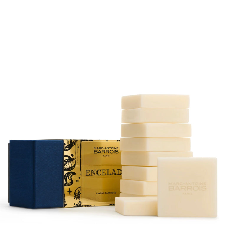 Marc-Antoine Barrois Encelad guest soap set, featuring a stack of cream-colored rectangular bars of soap, embossed with the brand name, and its gold and navy blue packaging box on a clean white background.