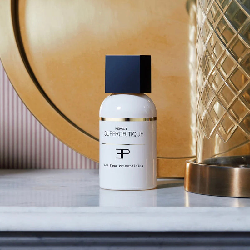 Néroli EdP - Supercritique Collection | Les Eaux Primordiales. White bottle with black cap on a marble surface with decorative background