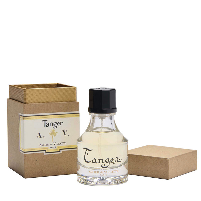 Tanger Parfum 1oz or 30ml bottle by Astier de Villatte.  Clear bottle with the writing "Tanger" containing the clear golden fragrance.  The cap is black. Next to it a brown paper box with the label that reads Tanger Astier de Villatte Paris and the initials A.V. with a golden palm tree symbol between the A. and V. 