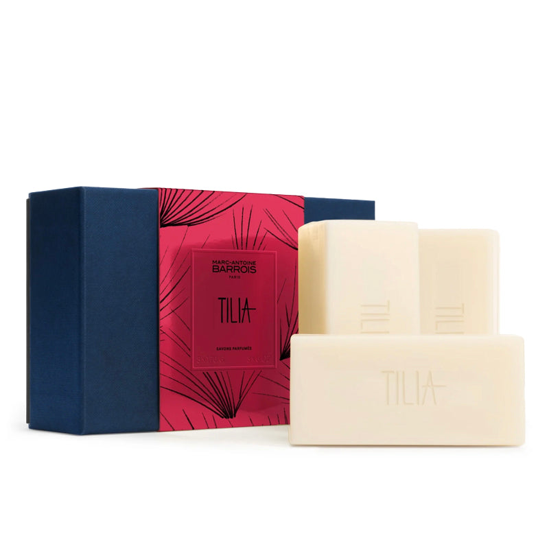 Three cream-colored TILIA luxury shampoo bars arranged in front of their navy blue and pink tropical-patterned gift box on a white background.